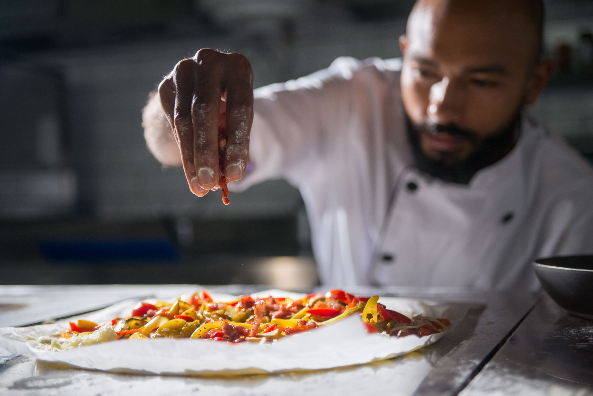 Pizzaiolo belegt een verse pizza in zijn keuken